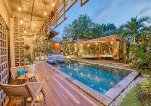 A pool area with wooden deck, lounge chairs, and a pergola with string lights. - Leafy Home Canggu (Canggu)