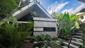 A modern building with a concrete facade, a visible cabin sign, and lush tropical vegetation. - Leafy Home Canggu (Canggu)