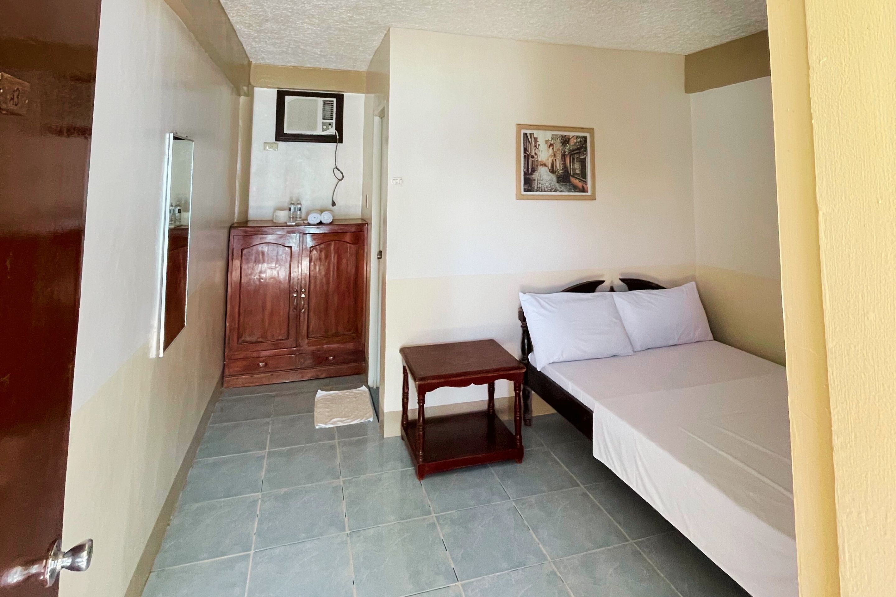 Una habitación pequeña y acogedora con cama, un armario de madera, una mesita y un espejo.