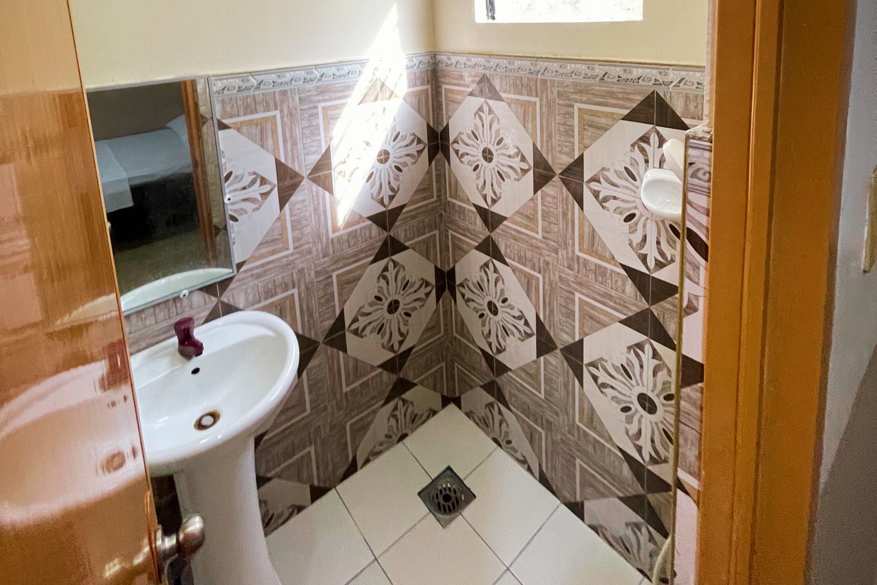 A bathroom with a white sink, a mirror, and patterned tile walls.