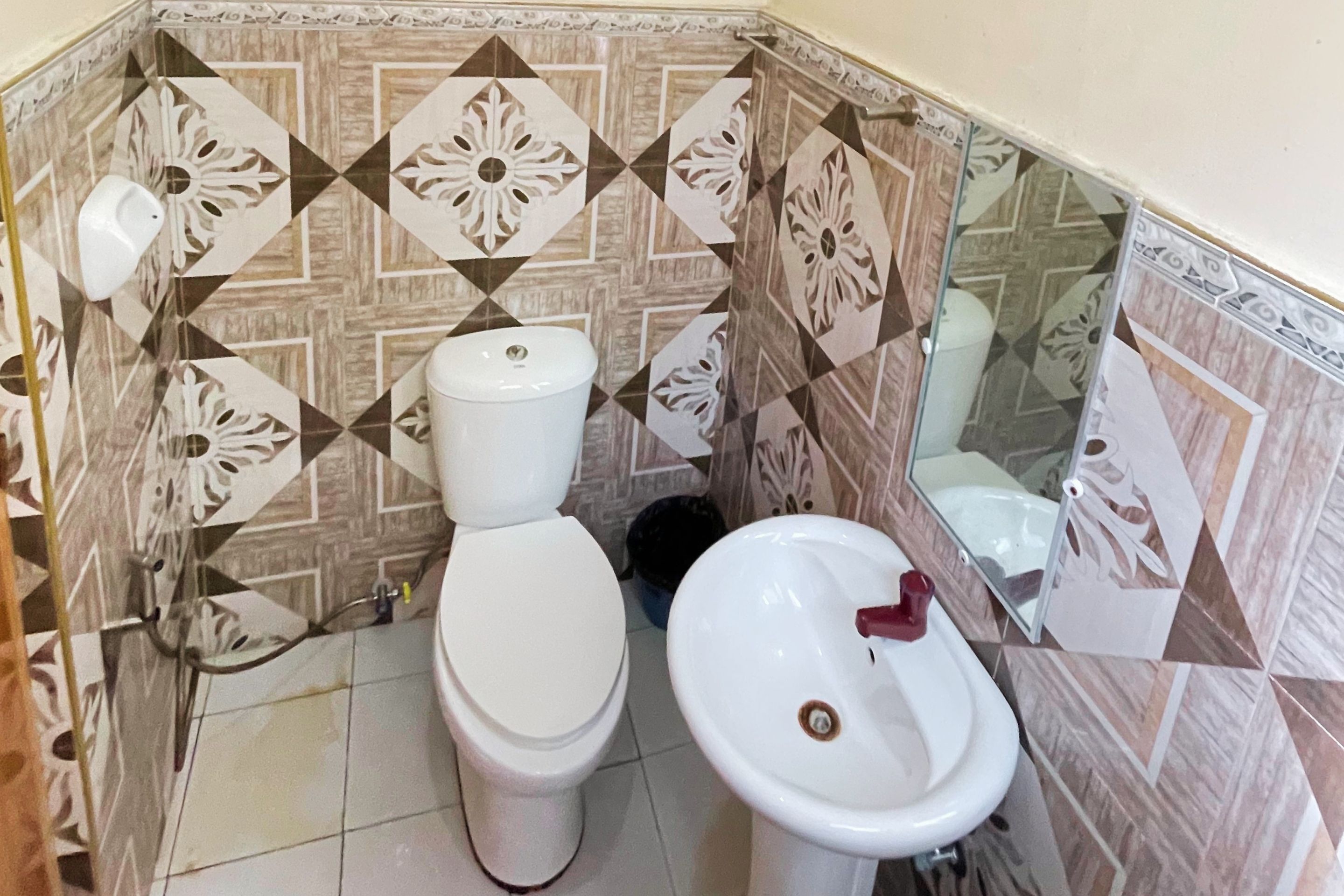 A bathroom with a toilet and sink, tiled walls with geometric patterns, and a mirror.