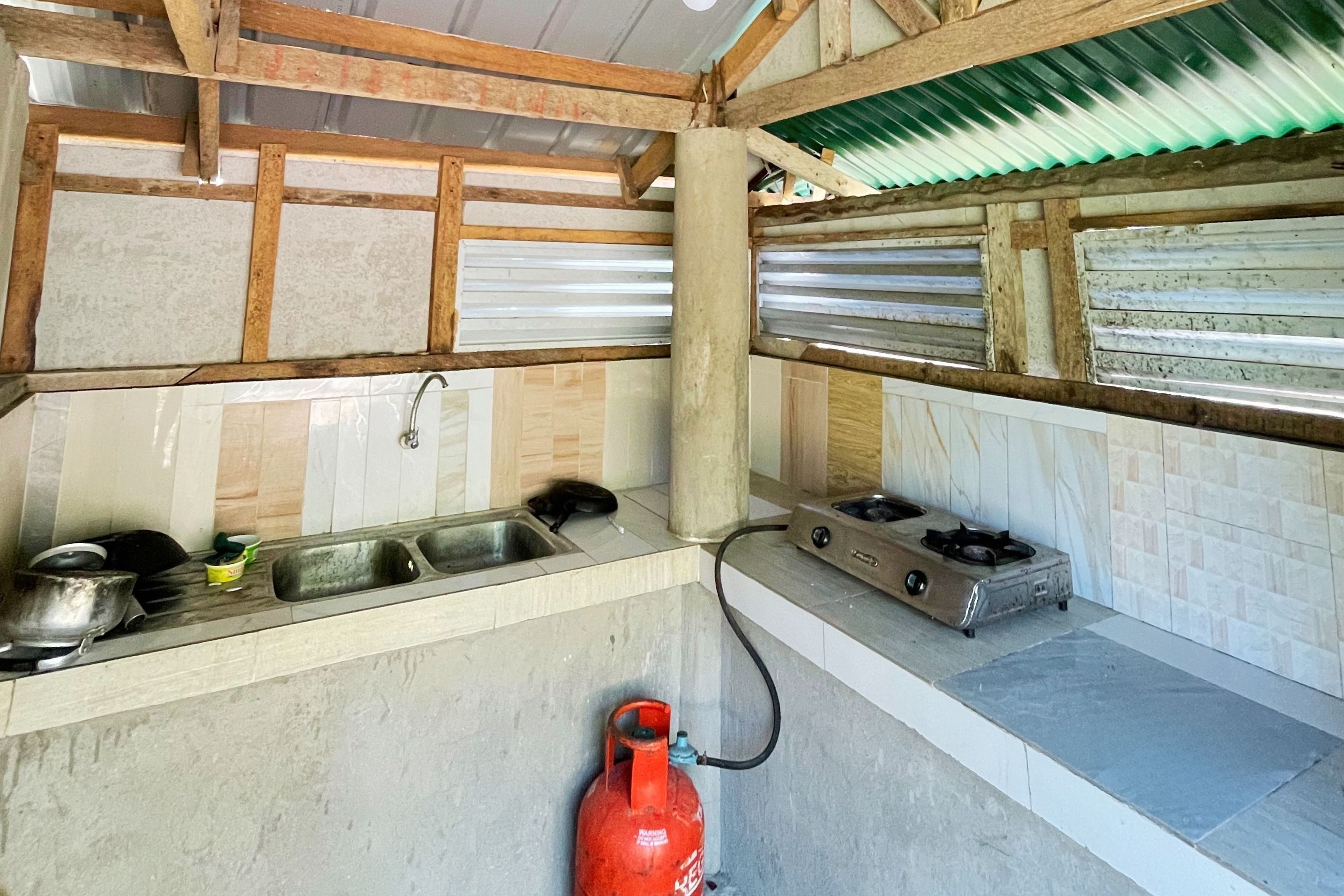 A kitchen with a gas stove, sink, and a red gas cylinder.