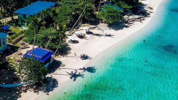 Un resort de playa tropical con aguas turquesas cristalinas, palmeras y varios edificios con techos azules.