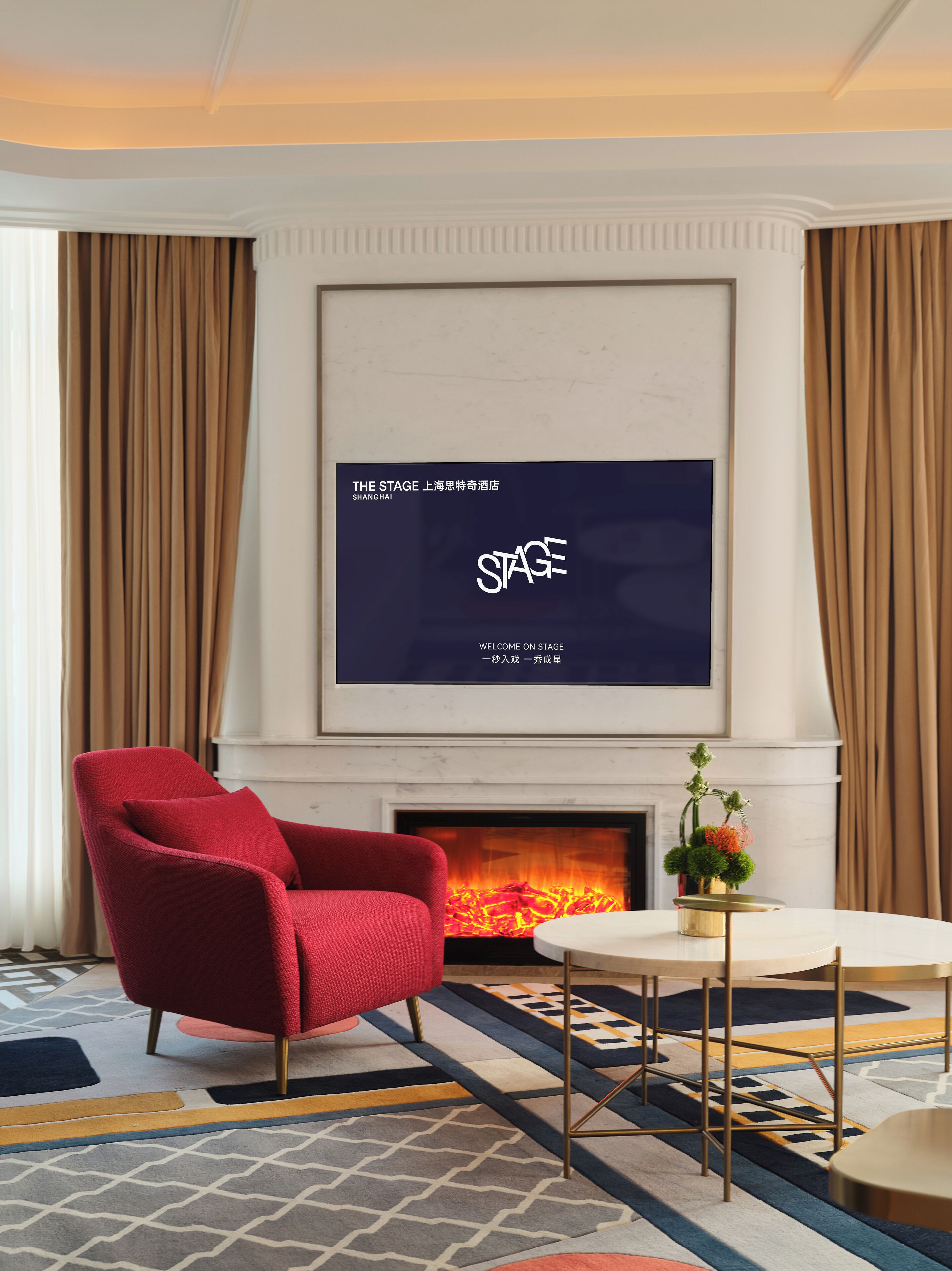 Una habitación de hotel moderna con un sillón rojo, una chimenea y una pantalla grande mostrando texto.