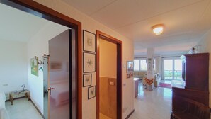 En rymlig hall med en trädörr, inramade tavlor på väggen och utsikt över ett vardagsrum med en soffa och ett fönster.