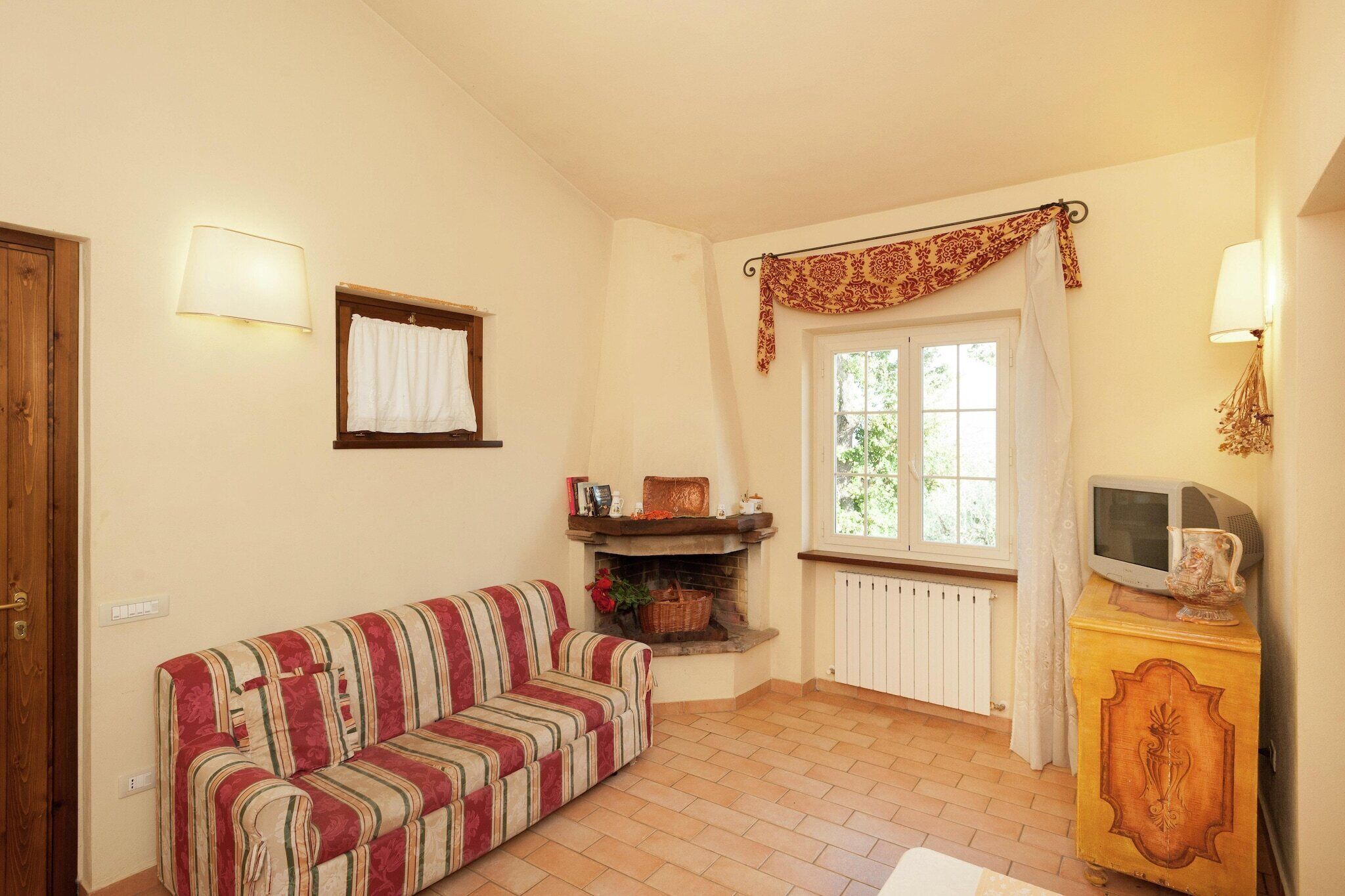 Una sala de estar acogedora con un sofá a rayas, una chimenea, un televisor sobre un mueble de madera y una ventana con cortinas.