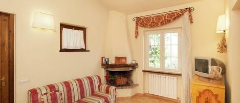 Una sala de estar acogedora con un sofá a rayas, una chimenea, un televisor sobre un mueble de madera y una ventana con cortinas.
