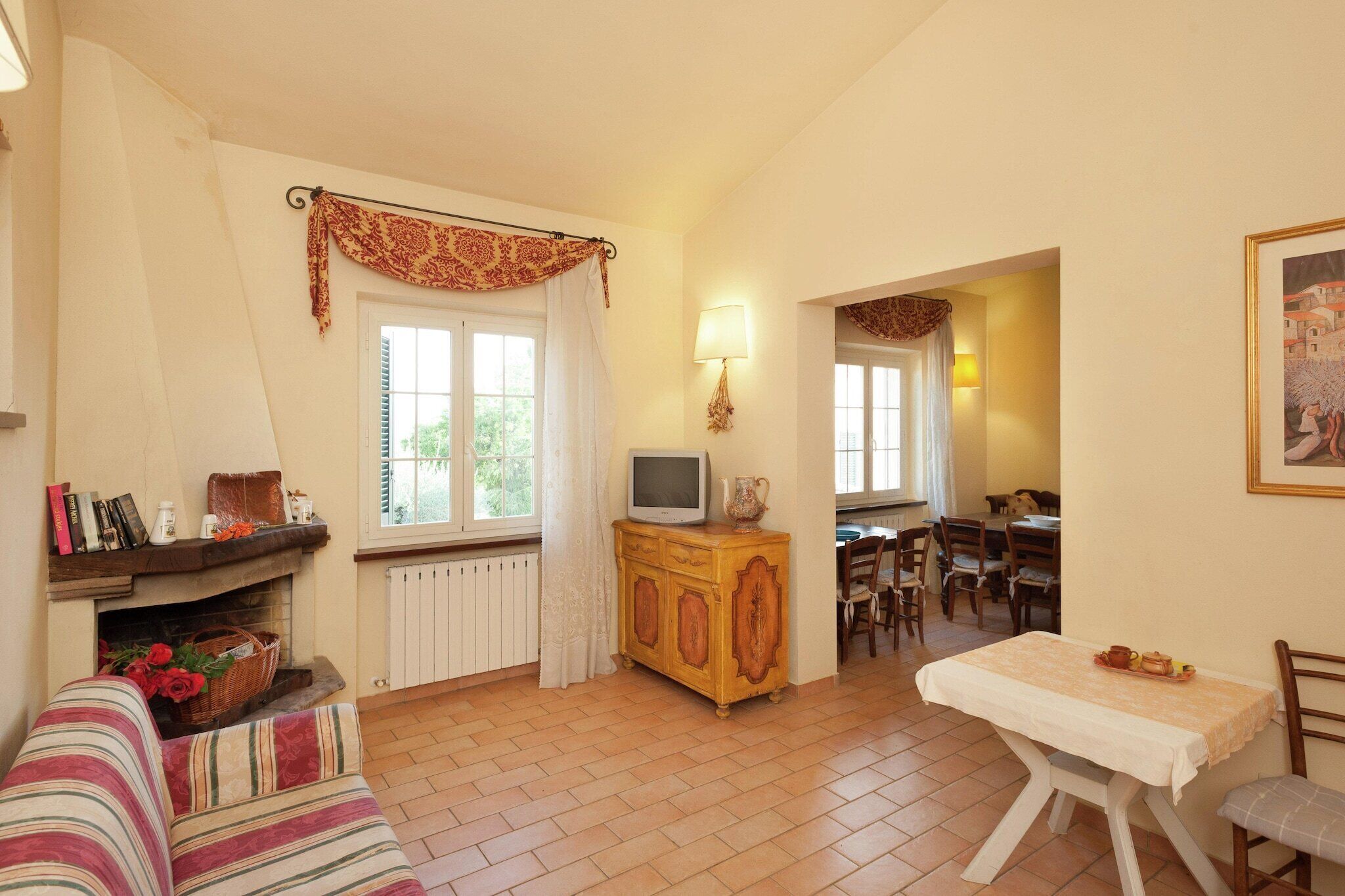 Una sala de estar acogedora con chimenea, un televisor sobre un mueble de madera, un comedor con sillas y una mesa con una bandeja de comida.