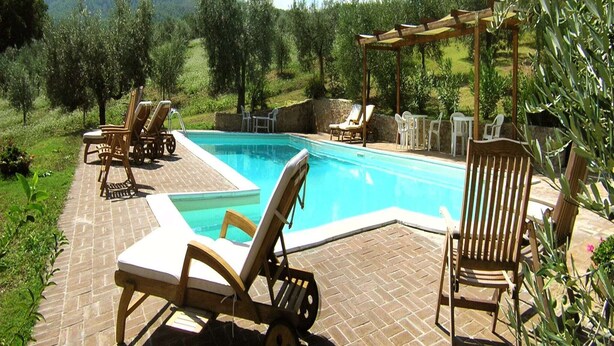 A pool area with lounge chairs and a pergola, surrounded by greenery and hills.