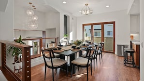 A spacious dining area with a long table, multiple chairs, and a modern chandelier.