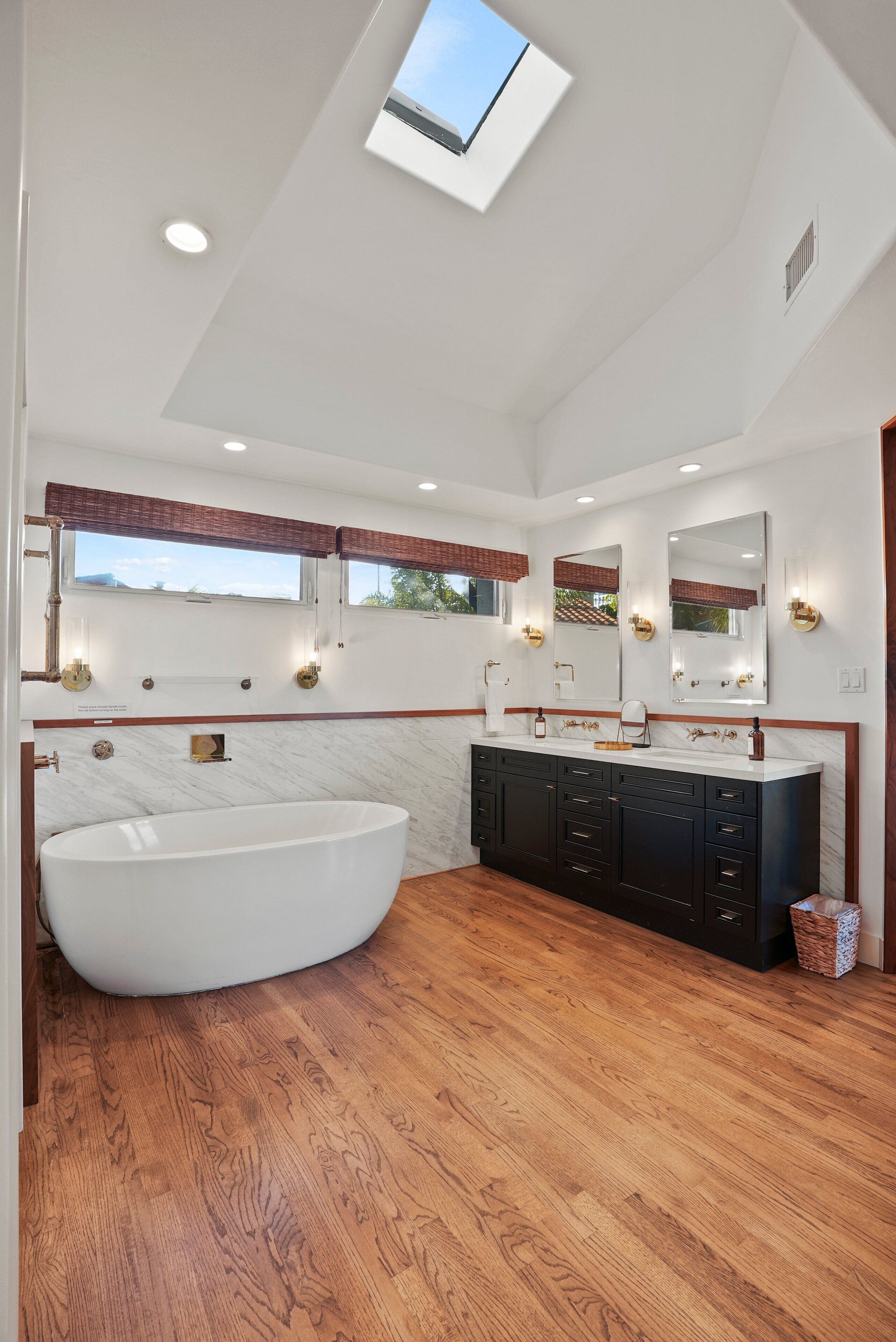 Ein modernes Badezimmer mit freistehender Badewanne, doppelter Waschtisch mit Spiegeln und einem Oberlicht.