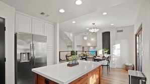 A modern kitchen with a central island, stainless steel appliances, wooden cabinetry, and a dining area with a chandelier.