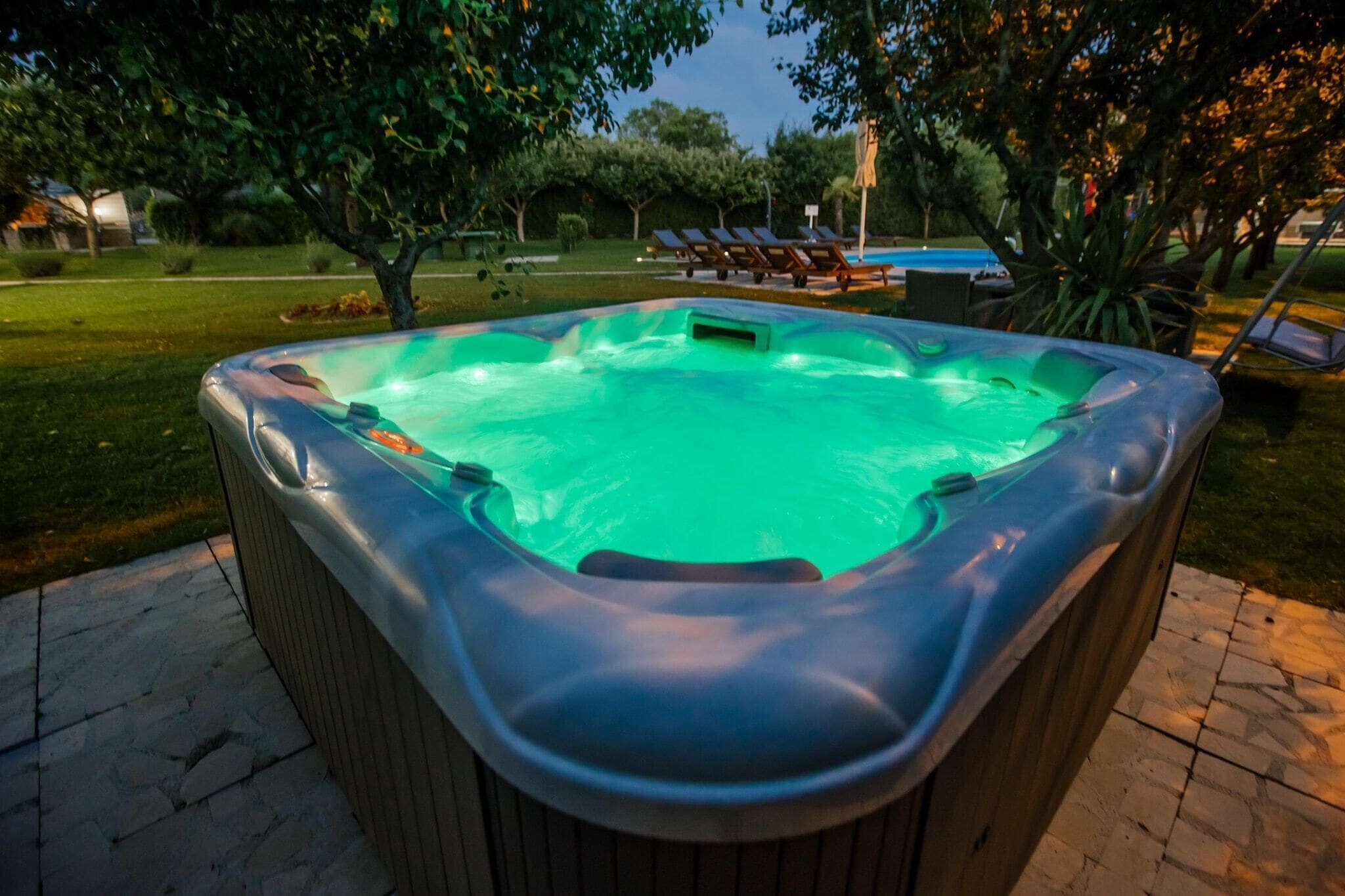A hot tub in an outdoor setting with a pool in the background.
