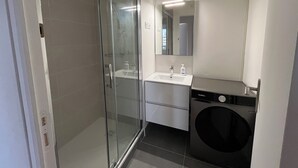 Ein modernes Badezimmer mit Duschkabine aus Glas, Waschbecken mit Spiegel und integriertem Waschmaschinenanschluss.