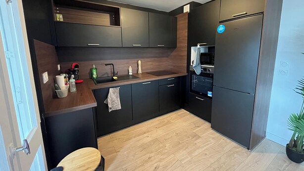 Eine moderne Küche mit dunklen Schränken, einer Holz Arbeitsplatte, einer Spüle, einer Mikrowelle und einem Kühlschrank.