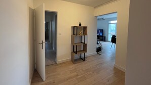 Ein Korridor mit Holzboden, der in einen Wohnbereich mit Fernseher, einem kleinen Tisch und einem Sessel führt.