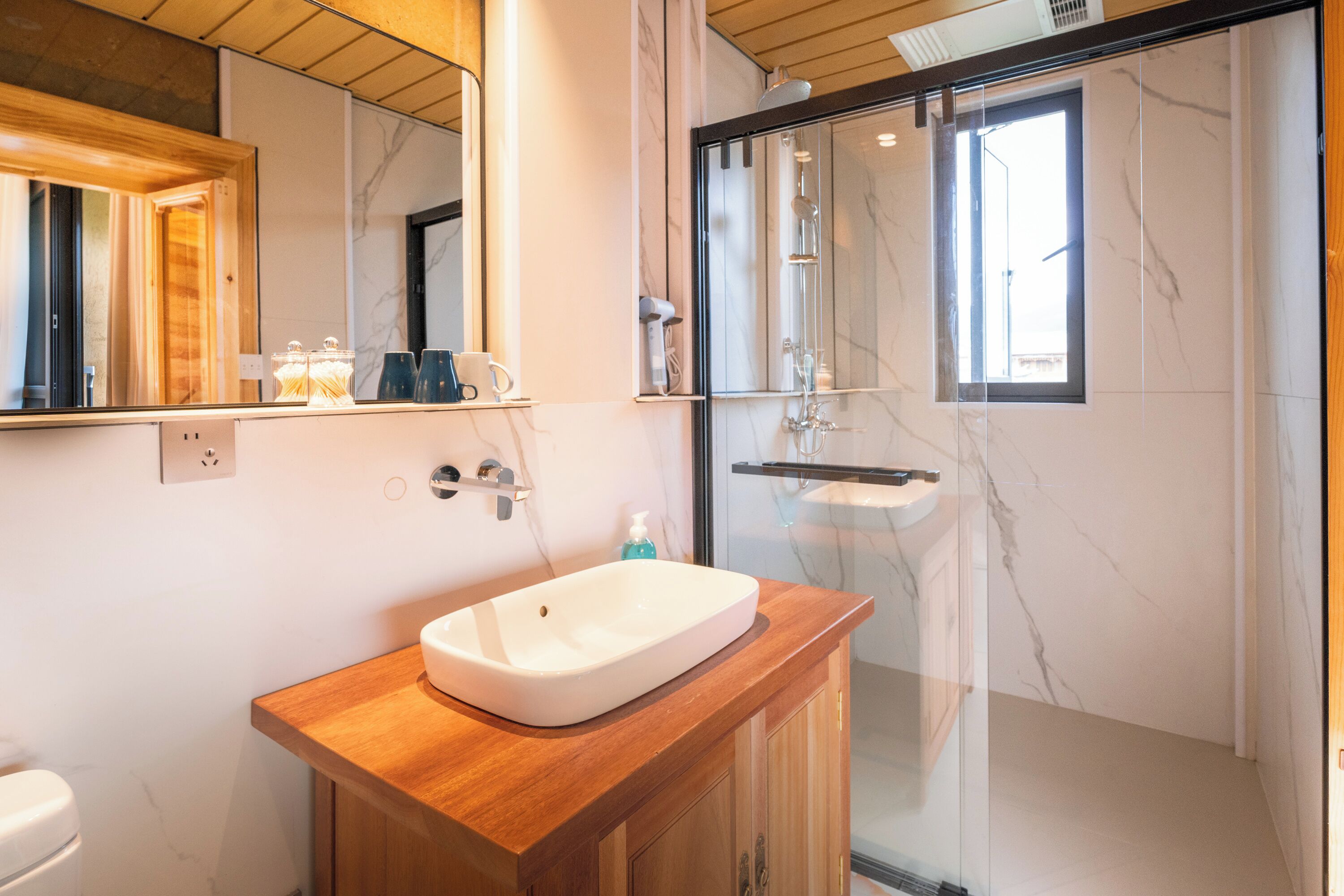 Un baño moderno con tocador de madera, un espejo grande, cabina de ducha de vidrio y paredes de mármol.