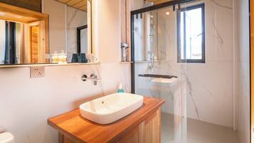 Un baño moderno con tocador de madera, un espejo grande, cabina de ducha de vidrio y paredes de mármol.