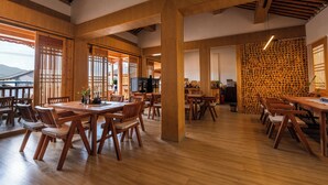 Une salle à manger spacieuse, dotée de tables et de chaises en bois, de grandes fenêtres et offrant une vue sur les montagnes.