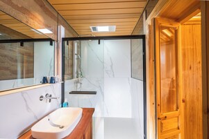 Un baño moderno con pared de mármol, tocador de madera, espejo grande y cabina de ducha de vidrio.