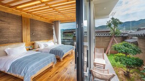 Une chambre avec deux lits, un plancher en bois et une vue sur une architecture traditionnelle, visible à travers une porte vitrée.