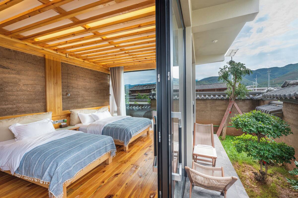 Une chambre avec deux lits, un plancher en bois et une vue sur une architecture traditionnelle, visible à travers une porte vitrée.