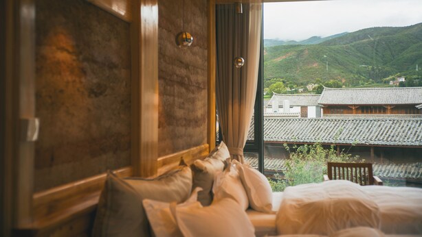 Une chambre avec un lit, des murs en bois et une vue sur des bâtiments traditionnels et des collines.