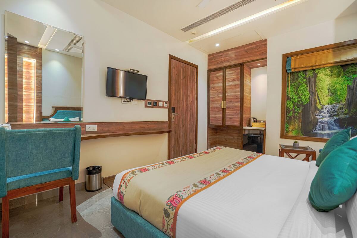 Ein Hotelzimmer mit Bett, Schreibtisch, Stuhl, Fernseher und einem Gemälde eines Wasserfalls.