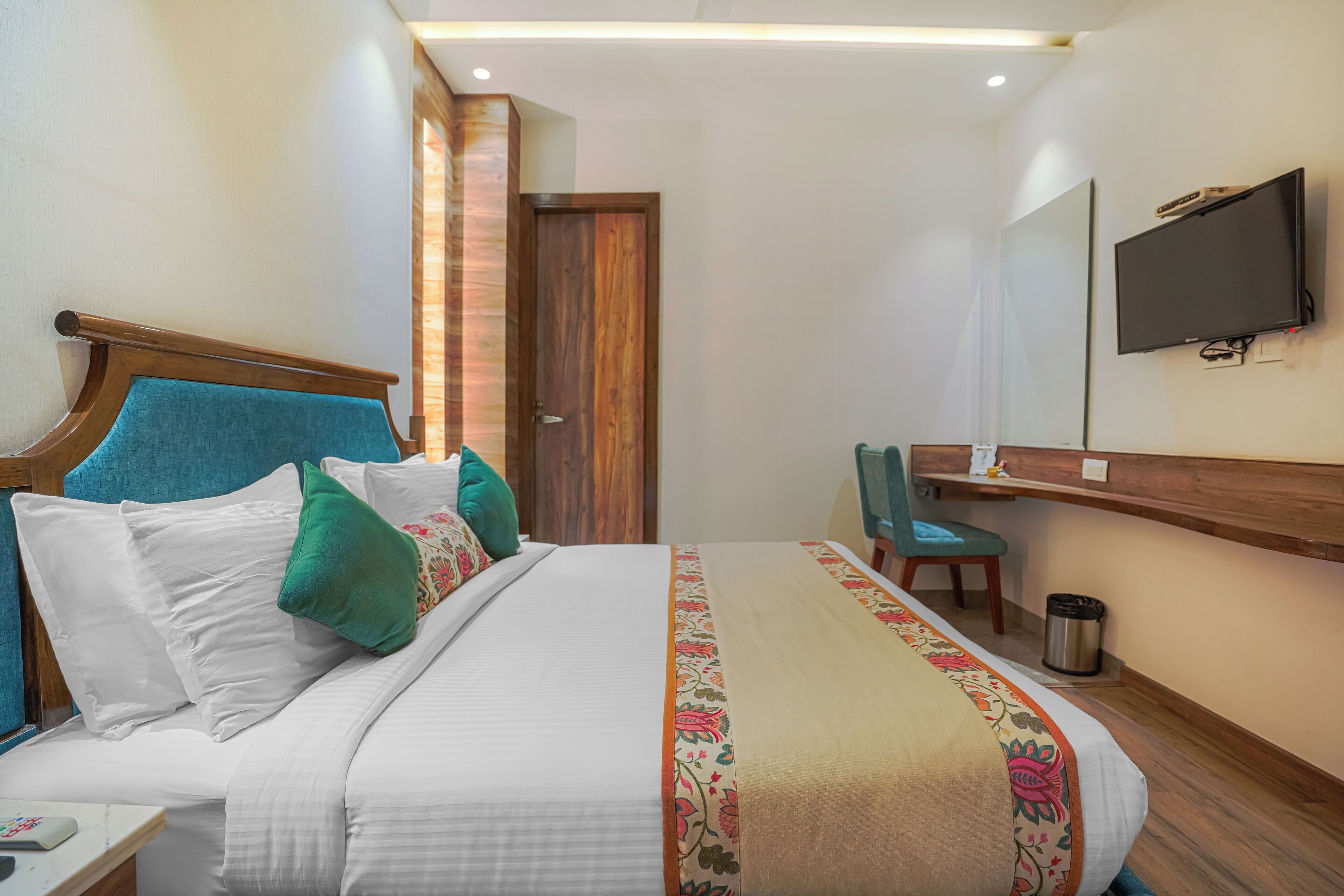 Una camera d'albergo con un letto, una scrivania, una sedia, una televisione e una porta.