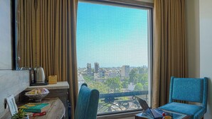Una habitación con un ventanal grande, una laptop sobre una mesita, una silla azul y un frutero en una estantería.