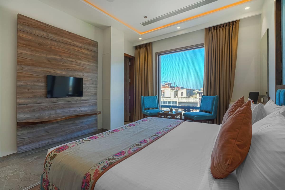 Ein Hotelzimmer mit einem großen Bett, einem flachbildfernseher, der an einer Holzplatte angebracht ist, einem kleinen Tisch mit Stühlen und Blick auf die Stadt durch große Fenster.