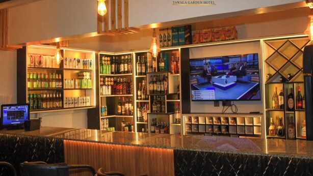 A bar area with shelves of liquor bottles, a television screen, and a laptop on a counter. - Tawala Garden Hotel (Nairobi)
