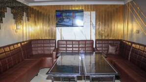 A room with a glass-top table, brown leather sofas, a TV on the wall, and a logo on the floor. - Tawala Garden Hotel (Nairobi)