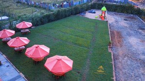 A grassy outdoor area with several red umbrellas and a small play structure. - Tawala Garden Hotel (Nairobi)