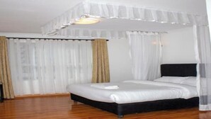 A bedroom with a four-poster bed, white bedding, and sheer curtains. - Tawala Garden Hotel (Nairobi)