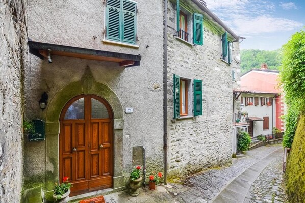 A narrow stone building with a wooden door and green shutters, number 22, with a cobblestone path and greenery. - Holiday Home Equi Terme near Karst Caves (Equi Terme)