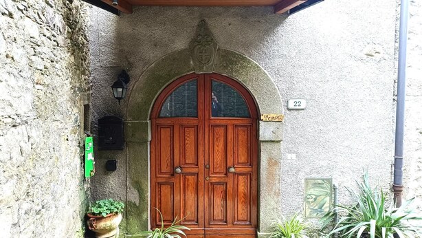 Une porte à deux battants en bois, surmontée d’un arc en pierre, avec une enseigne verte et un pot de fleurs.