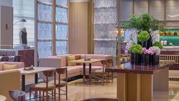 Un área de descanso moderna con mesas redondas, asientos acolchados, un centro de mesa con planta decorativa y un bar al fondo.