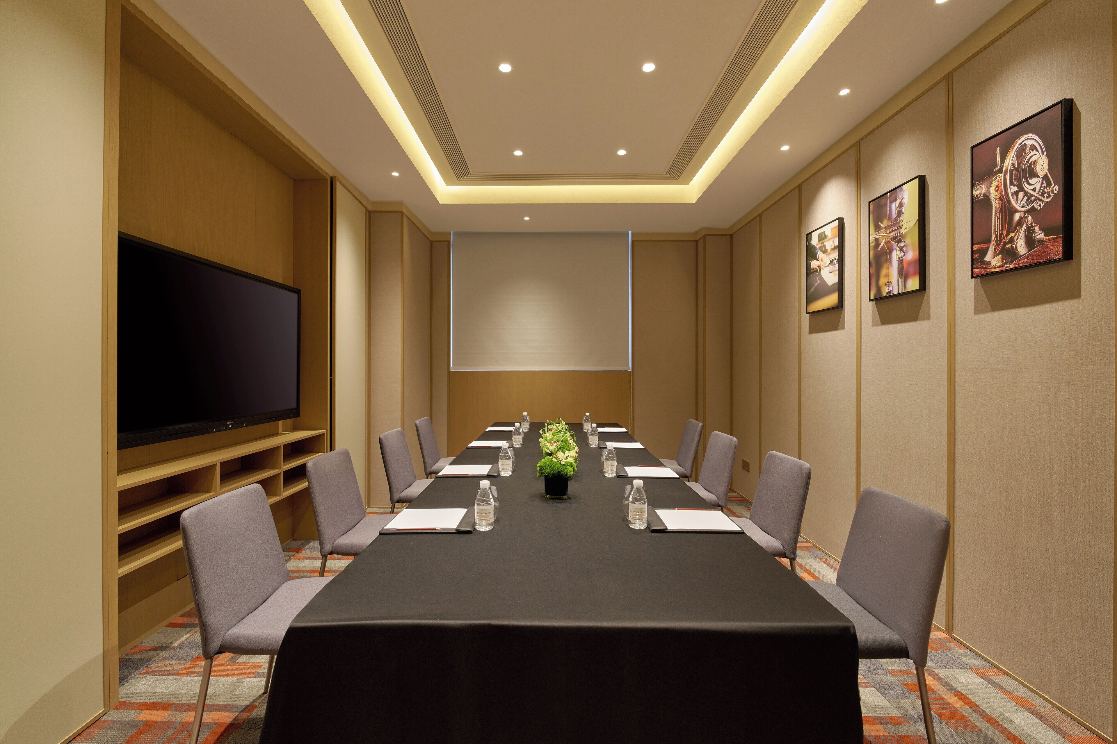 A conference room with a long table, chairs, a projector screen, and a television.