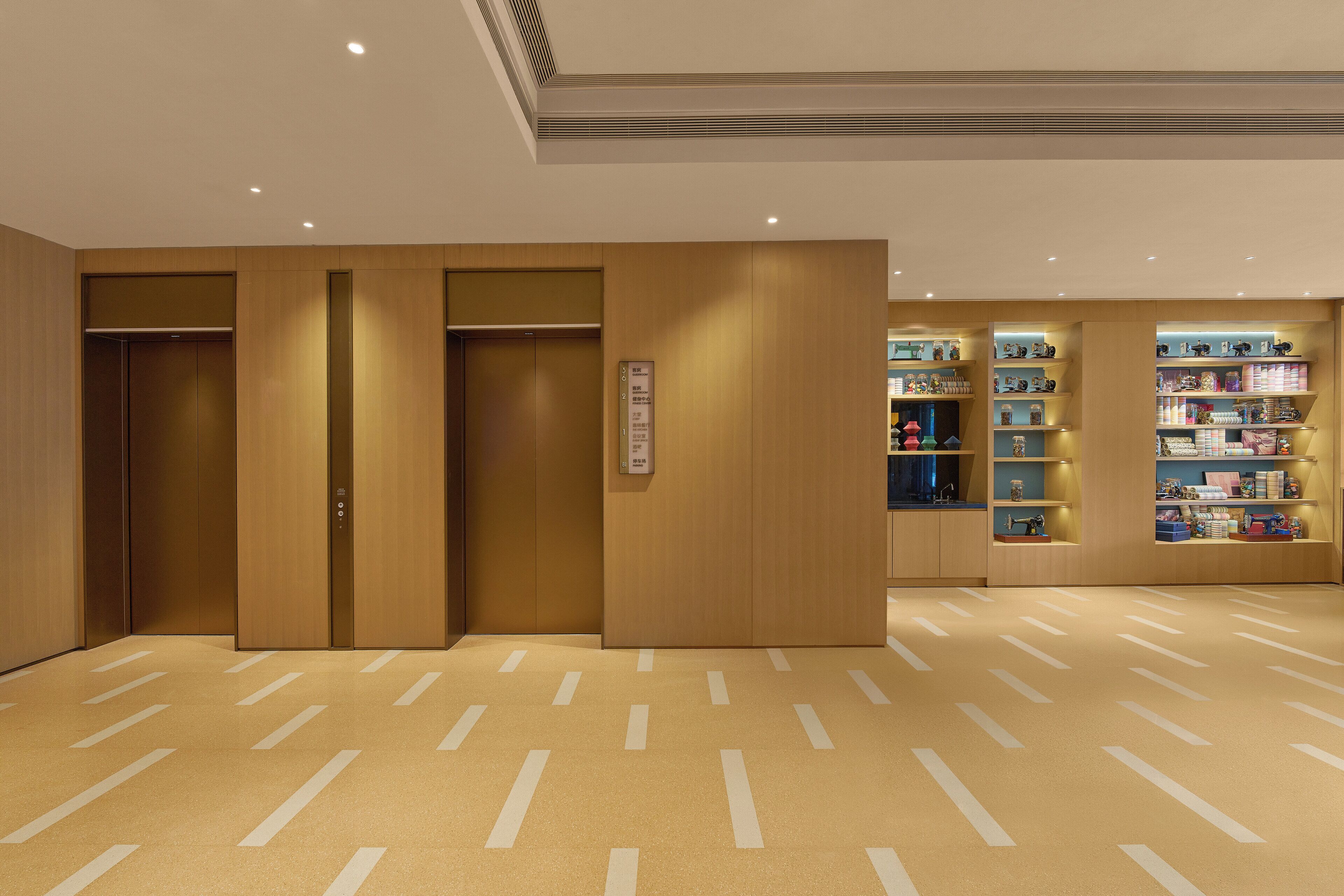 Egy hotel hallja, ahol három lift, egy recepciós pult és polcokon elhelyezett, különböző tárgyak találhatók.