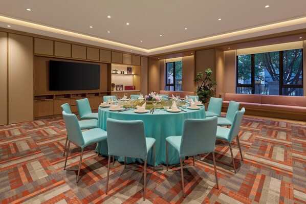 Een vergaderruimte met een ronde tafel, lichtblauwe stoelen en een groot televisiescherm.