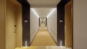Un couloir d’hôtel moderne avec des portes en bois, un sol recouvert de moquette et un éclairage encastré.