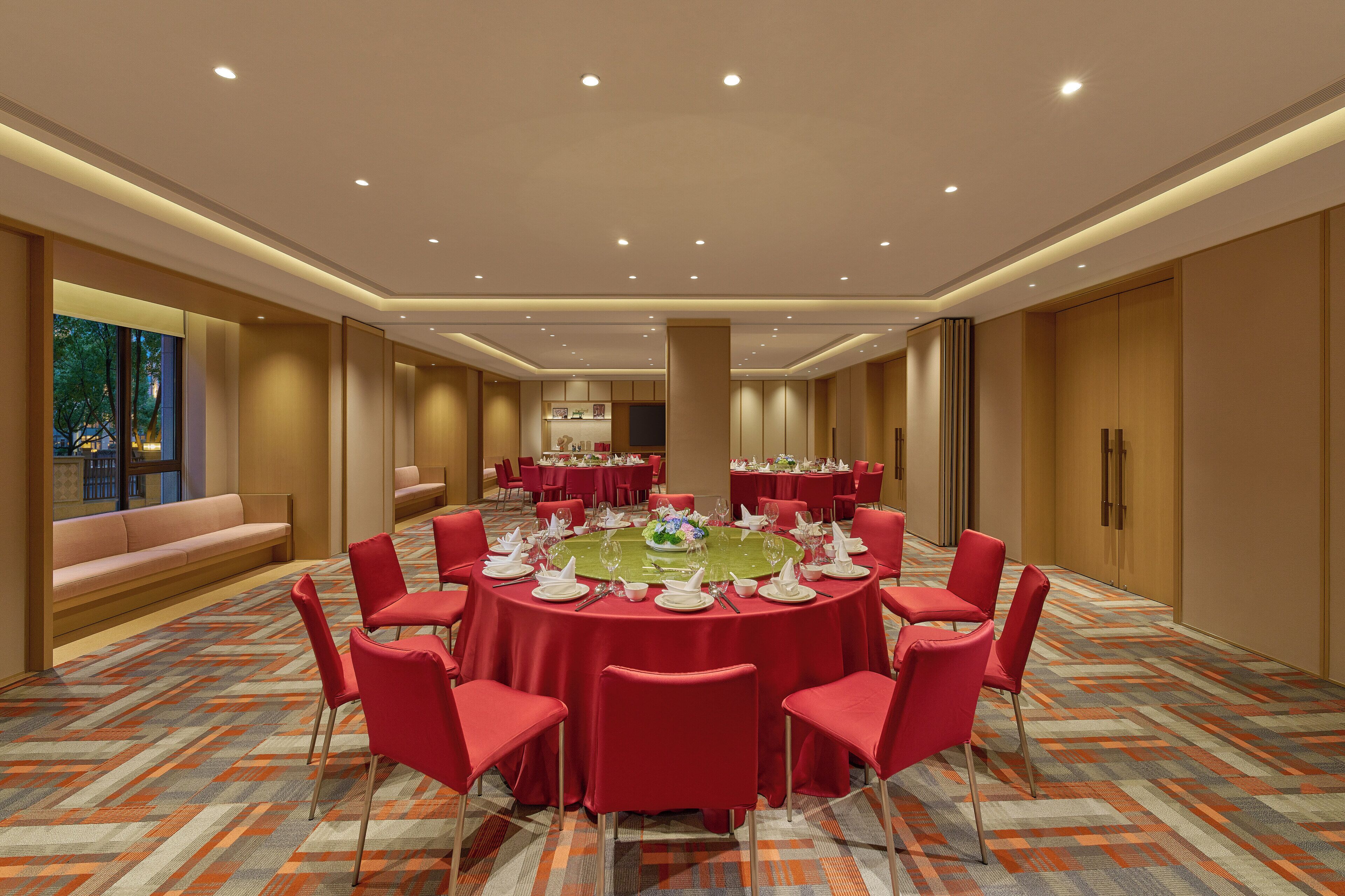 A conference room with a round table, red chairs, and a patterned carpet.