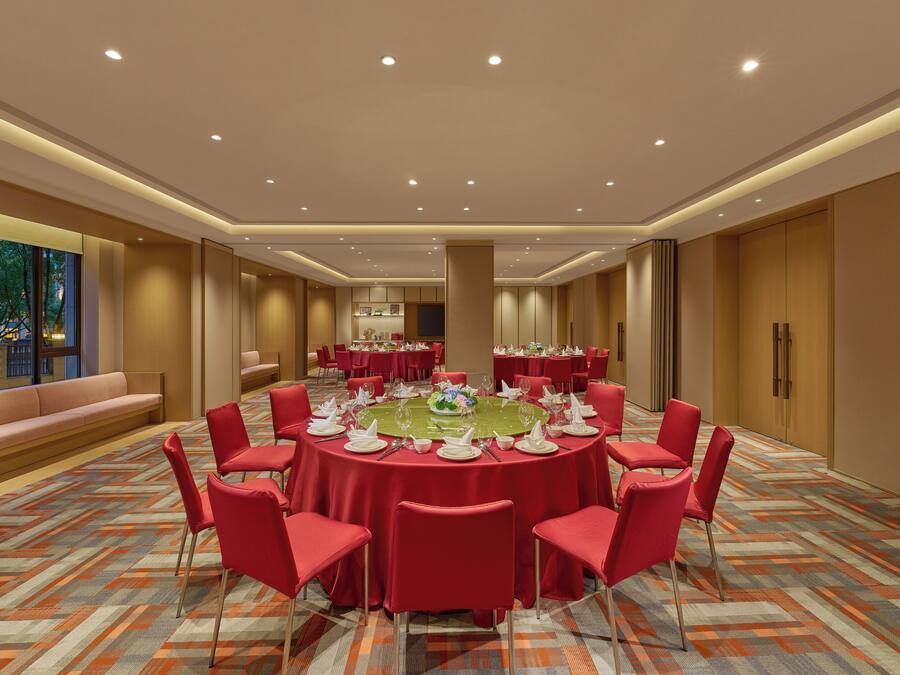 A conference room with a round table, red chairs, and a patterned carpet.