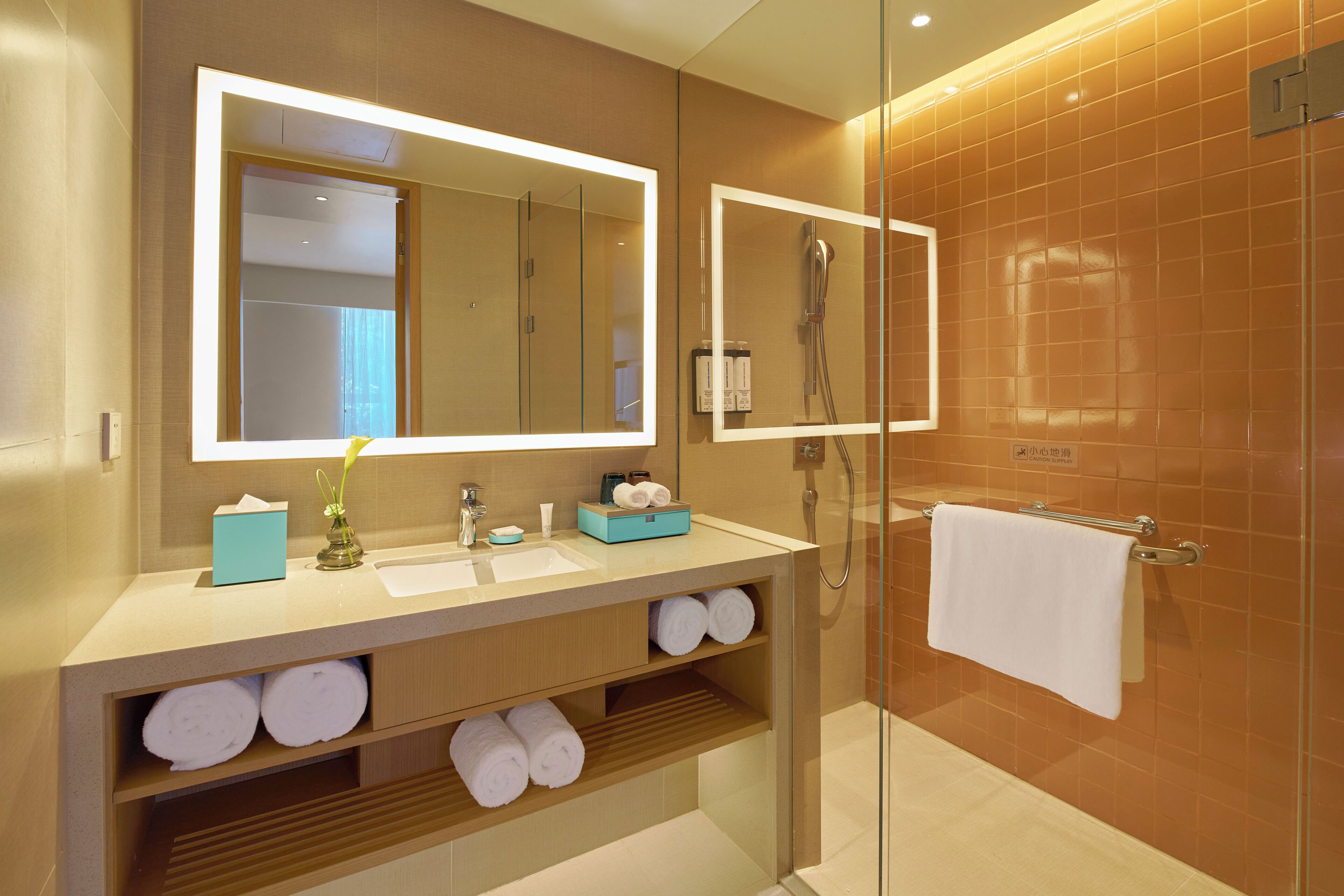 A modern bathroom with a large mirror, a glass-enclosed shower, and neatly arranged towels.