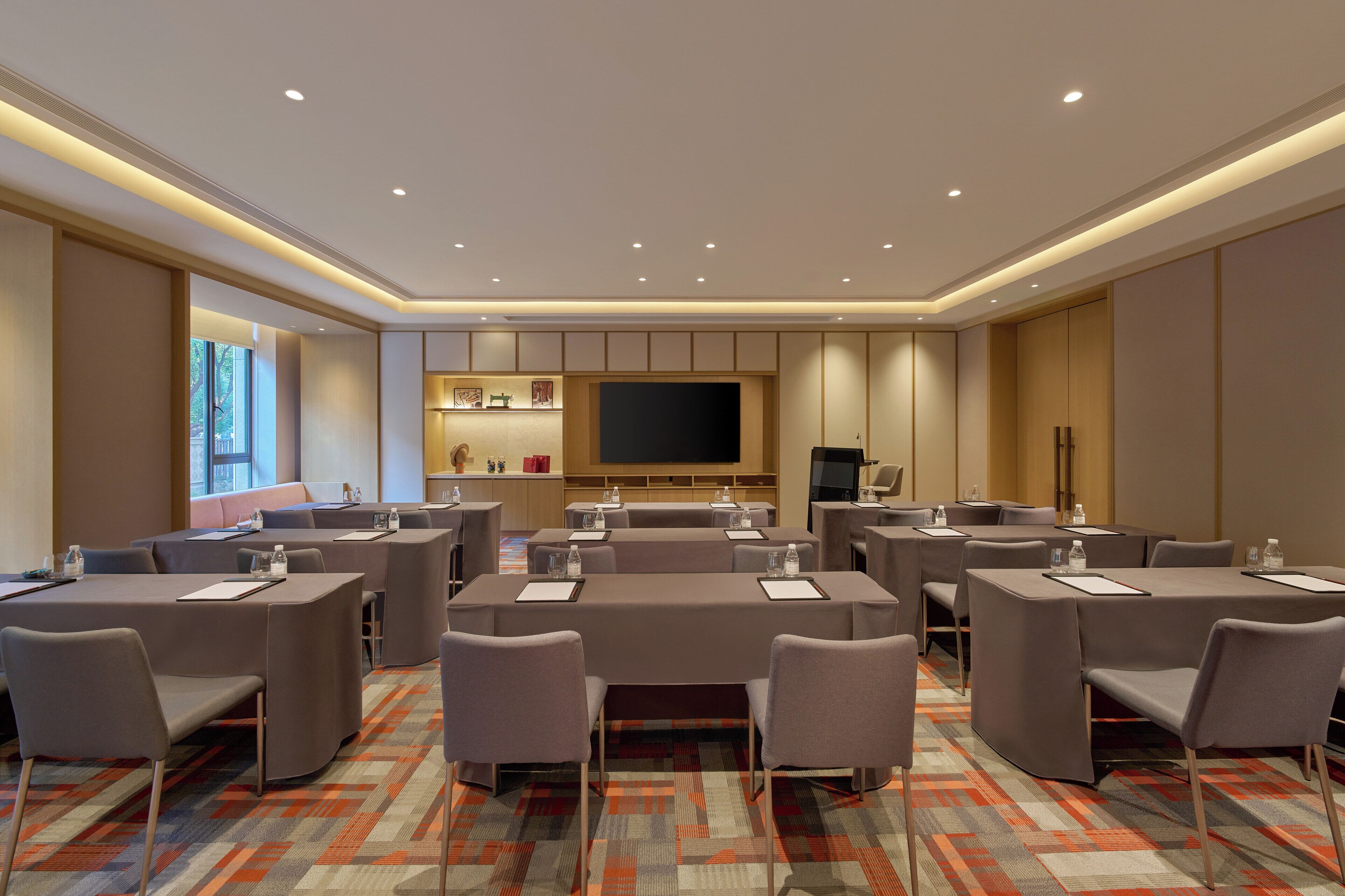 A conference room with multiple tables and chairs, a large flat-screen TV, and a small kitchenette area.