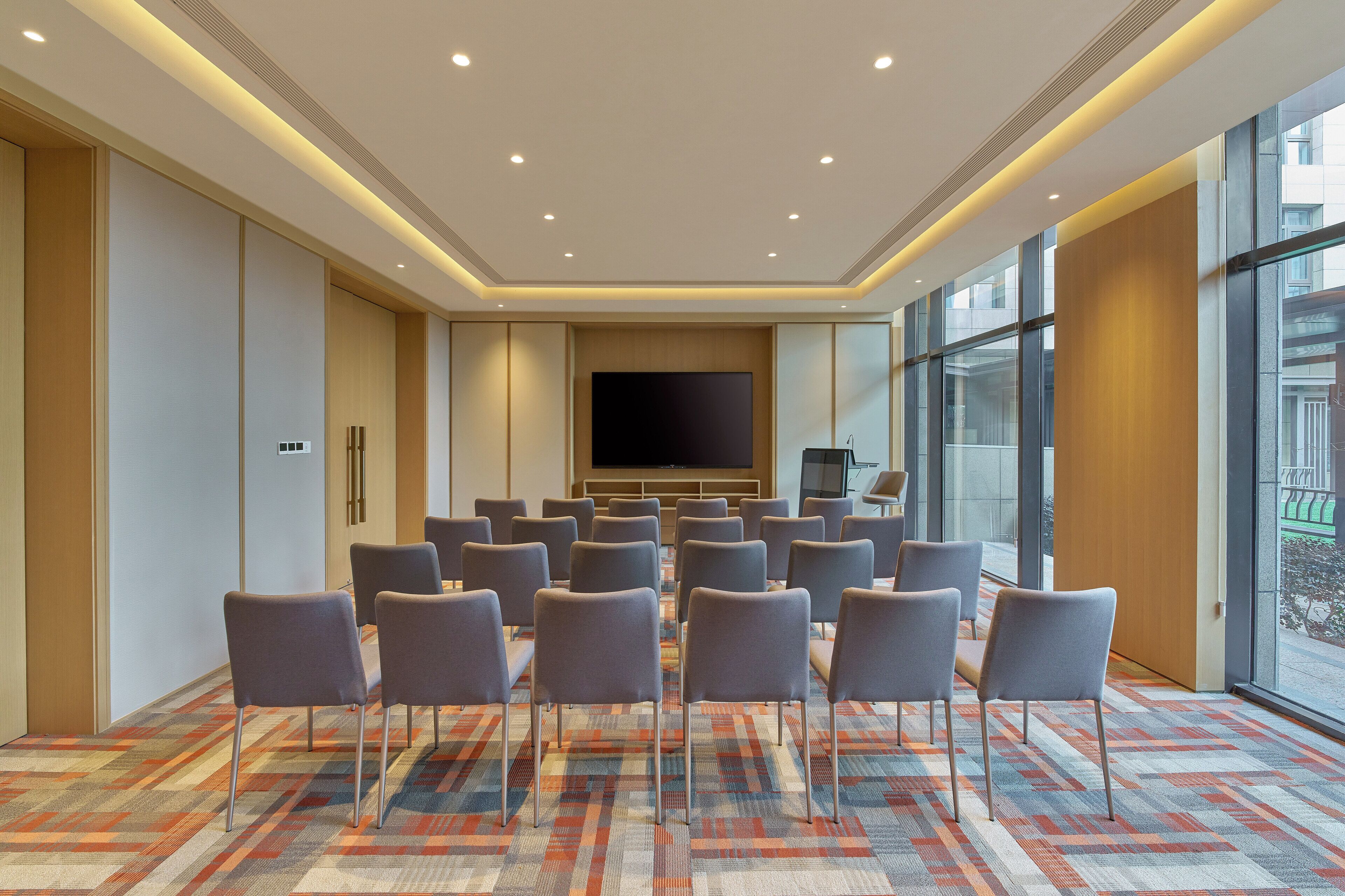 A conference room with a large screen, rows of chairs, and a patterned carpet.