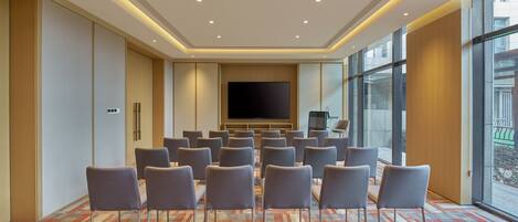 A conference room with a large screen, rows of chairs, and a patterned carpet.