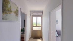 Un pasillo con una puerta que da a una habitación, una unidad de aire acondicionado sobre la puerta y un cuadro en la pared.
