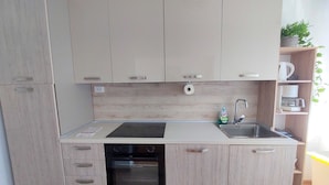 Una cocina moderna con armarios de madera clara, horno empotrado, pileta y encimera con dispensador de jabón.